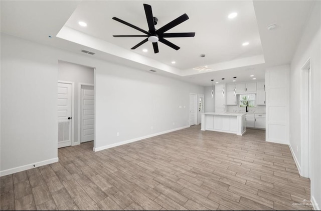 unfurnished living room with light hardwood / wood-style flooring, a raised ceiling, and ceiling fan