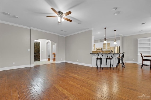 unfurnished living room with wood-type flooring, ornamental molding, and ceiling fan