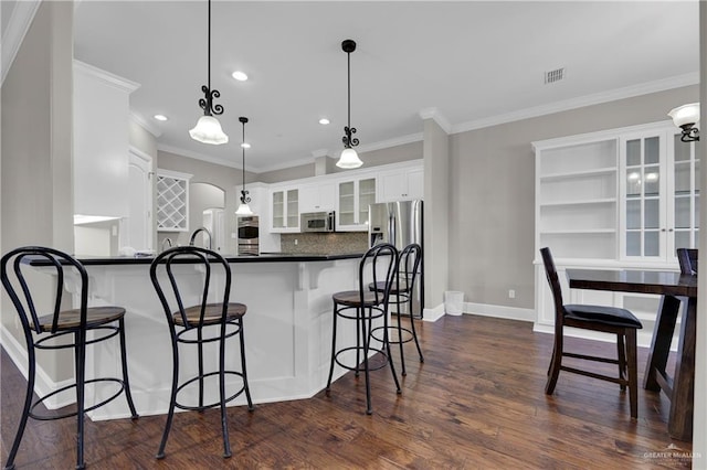 kitchen with dark wood-type flooring, appliances with stainless steel finishes, white cabinetry, hanging light fixtures, and a kitchen breakfast bar