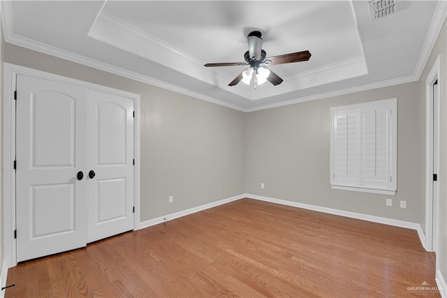 unfurnished bedroom featuring a raised ceiling, ornamental molding, ceiling fan, and light hardwood / wood-style flooring