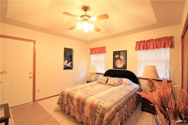 carpeted bedroom with a raised ceiling, ceiling fan, and a textured ceiling