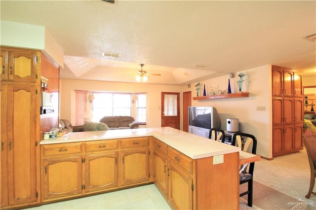 kitchen featuring a breakfast bar, a textured ceiling, a tray ceiling, kitchen peninsula, and ceiling fan