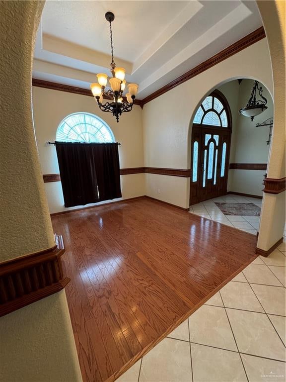 entrance foyer featuring a chandelier, a tray ceiling, light hardwood / wood-style flooring, and ornamental molding