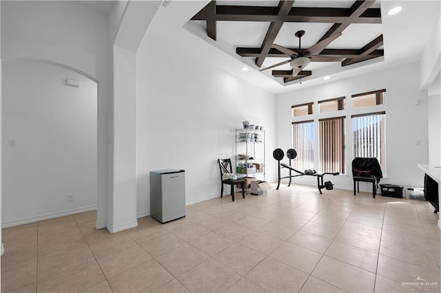 workout room featuring light tile patterned flooring, coffered ceiling, ceiling fan, and a towering ceiling