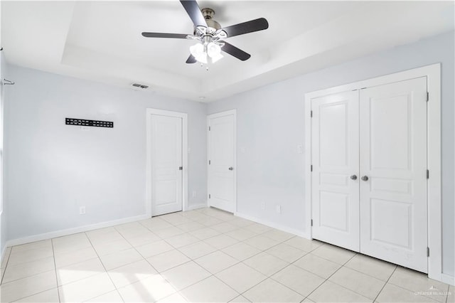 unfurnished bedroom with light tile patterned floors, visible vents, a raised ceiling, and baseboards