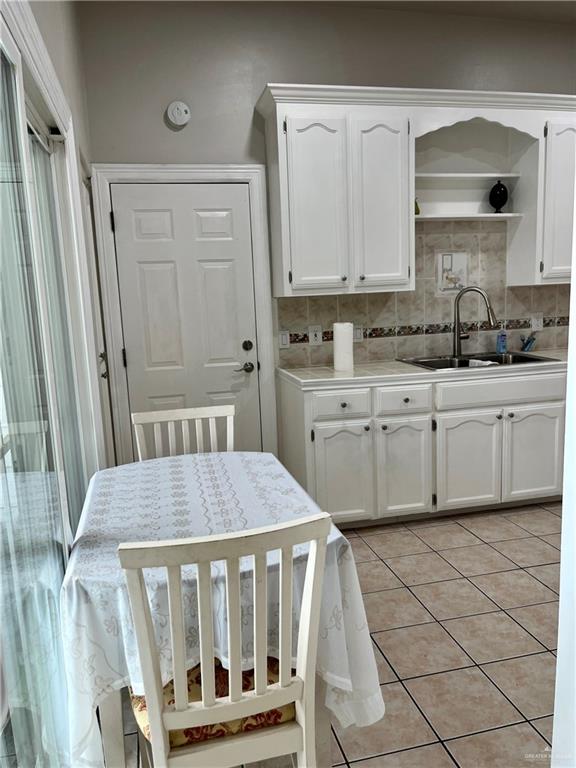 kitchen with light tile patterned floors, tasteful backsplash, white cabinetry, and sink