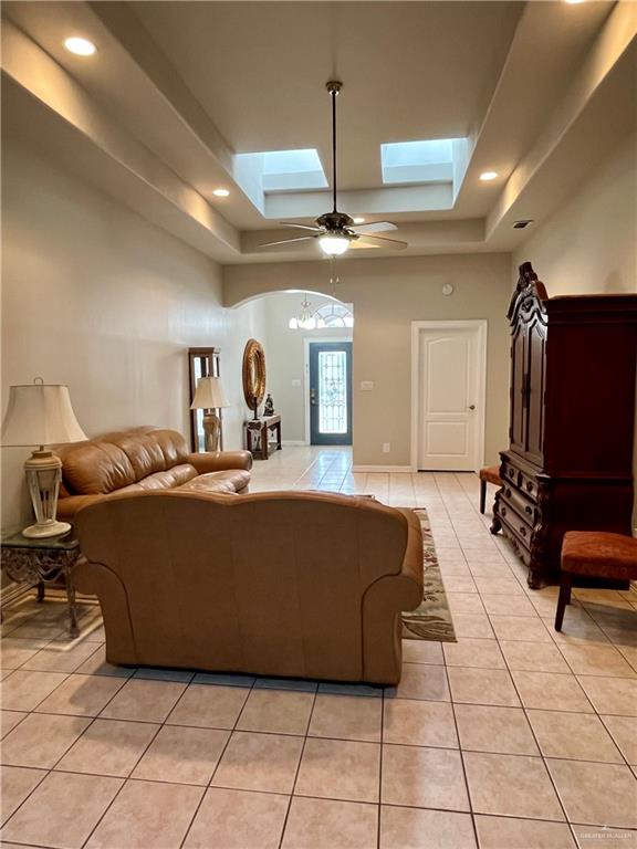 tiled living room featuring a raised ceiling, a skylight, and ceiling fan