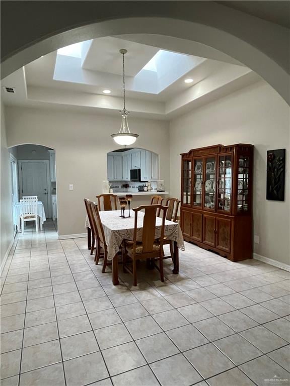 dining space with a high ceiling, a tray ceiling, light tile patterned floors, and a skylight