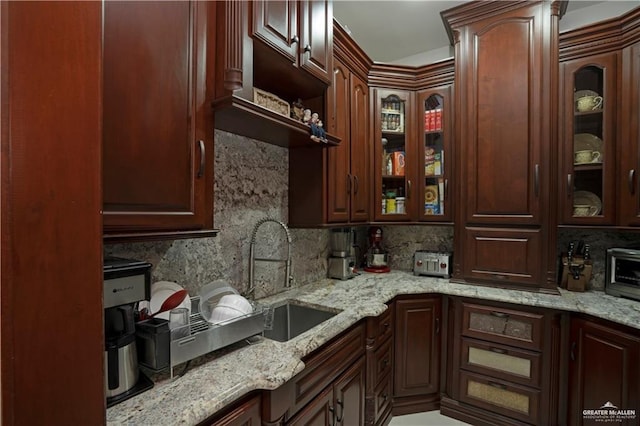 kitchen featuring light stone counters, dark brown cabinetry, sink, and tasteful backsplash