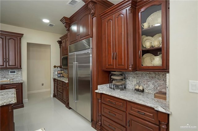 kitchen featuring light tile patterned floors, tasteful backsplash, stainless steel built in fridge, and light stone counters