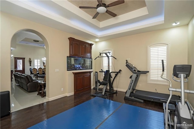 workout area featuring a tray ceiling, ceiling fan, and dark wood-type flooring