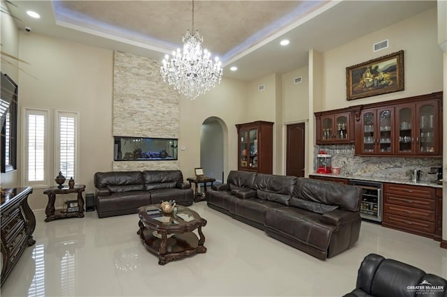 tiled living room with bar area, a high ceiling, wine cooler, and a notable chandelier