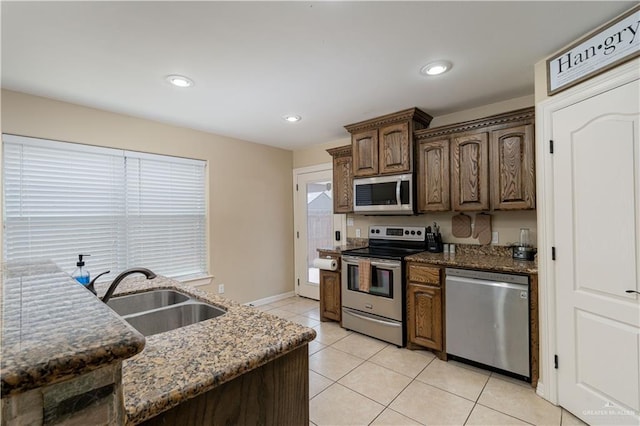 kitchen featuring light tile patterned floors, dark stone countertops, stainless steel appliances, and a sink