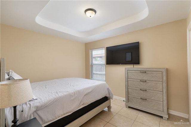 bedroom with light tile patterned floors, a tray ceiling, and baseboards