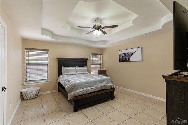 bedroom with a tray ceiling, light tile patterned flooring, a ceiling fan, and baseboards