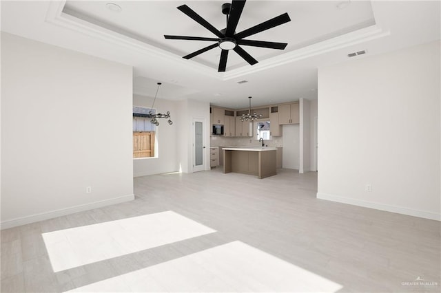 unfurnished living room featuring ceiling fan with notable chandelier, light hardwood / wood-style flooring, and a raised ceiling