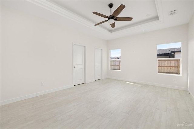 empty room with a tray ceiling, ceiling fan, and light wood-type flooring