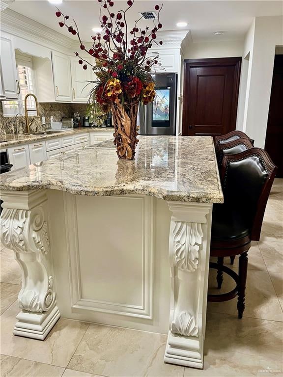 kitchen with a kitchen bar, light stone countertops, tasteful backsplash, white cabinets, and a large island