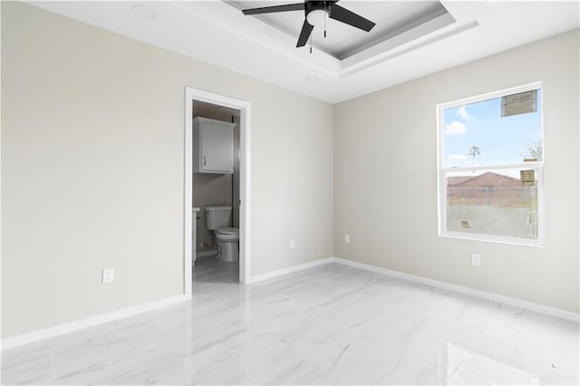 unfurnished bedroom with ensuite bathroom, ceiling fan, and a tray ceiling