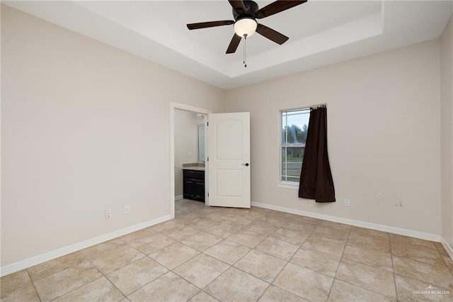 unfurnished bedroom featuring ceiling fan, light tile patterned flooring, ensuite bath, and a tray ceiling