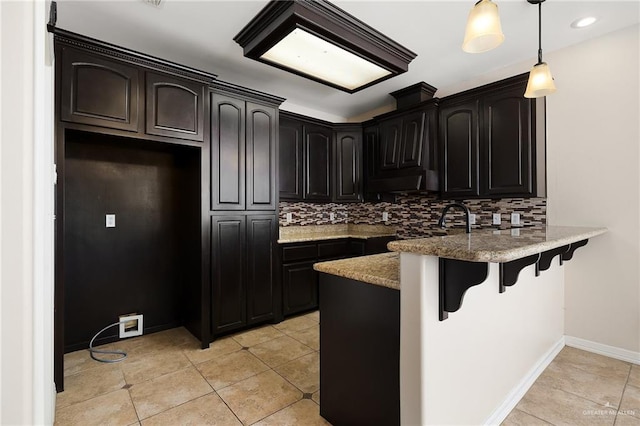 kitchen featuring light tile patterned floors, tasteful backsplash, decorative light fixtures, kitchen peninsula, and a breakfast bar area