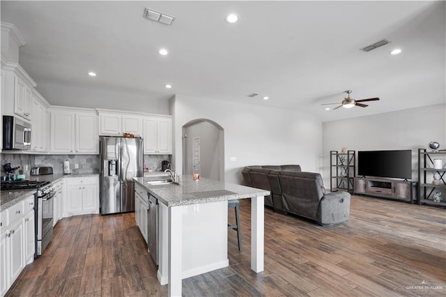 kitchen featuring light stone countertops, a breakfast bar, stainless steel appliances, a kitchen island with sink, and white cabinets