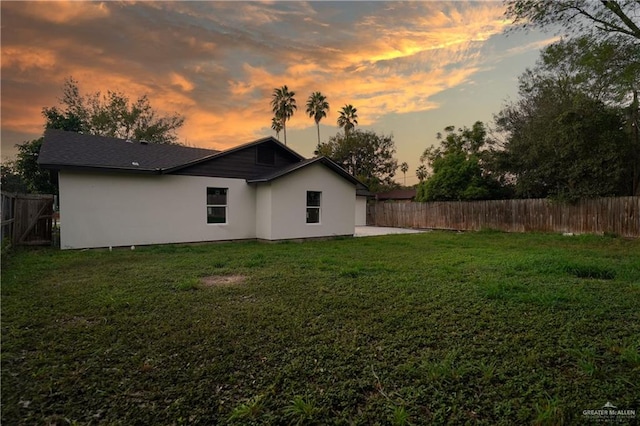 back house at dusk featuring a yard and a patio