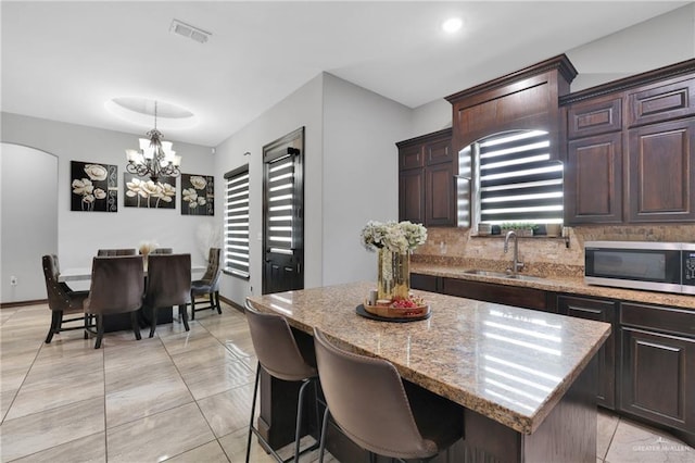 kitchen featuring stainless steel microwave, dark brown cabinets, a center island, a sink, and visible vents