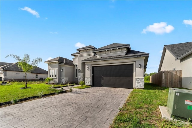 prairie-style home featuring a garage, fence, stone siding, decorative driveway, and a front lawn