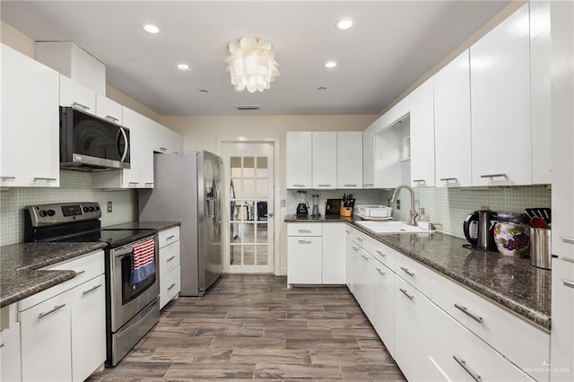 kitchen with dark stone counters, stainless steel appliances, sink, dark hardwood / wood-style floors, and white cabinetry