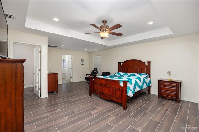 bedroom with dark hardwood / wood-style flooring, a tray ceiling, ceiling fan, and connected bathroom