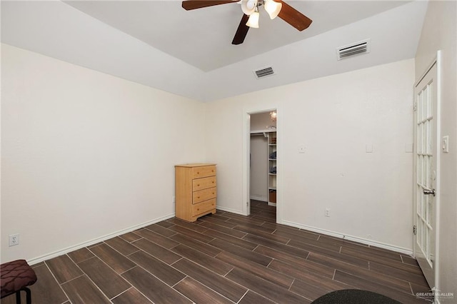 unfurnished bedroom featuring ceiling fan, a walk in closet, dark wood-type flooring, and a closet