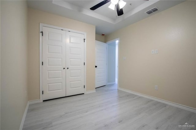 unfurnished bedroom with a raised ceiling, light wood-type flooring, ceiling fan, and a closet