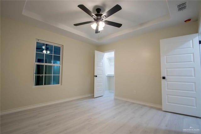 empty room featuring ceiling fan, light wood-type flooring, and a raised ceiling