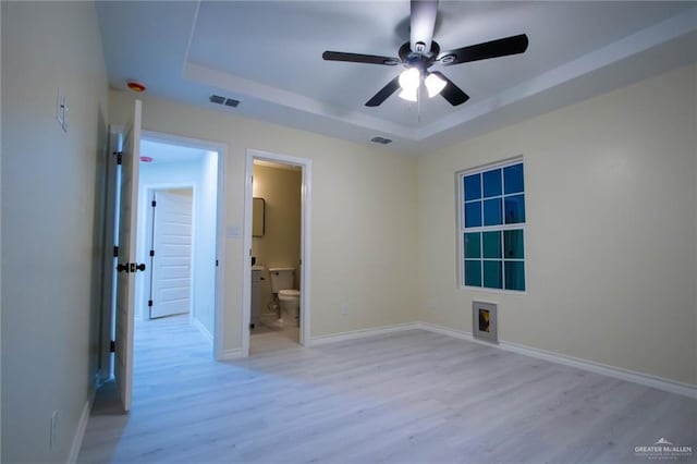 unfurnished bedroom with ensuite bathroom, light hardwood / wood-style flooring, ceiling fan, and a tray ceiling