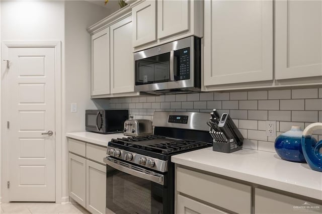 kitchen featuring light tile patterned flooring, appliances with stainless steel finishes, decorative backsplash, and white cabinets