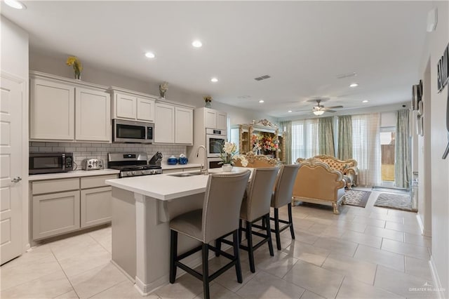 kitchen featuring sink, a breakfast bar area, backsplash, stainless steel appliances, and a center island with sink