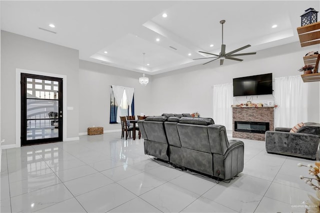 living room featuring ceiling fan, a raised ceiling, and a fireplace