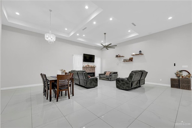 living room featuring a raised ceiling and ceiling fan with notable chandelier