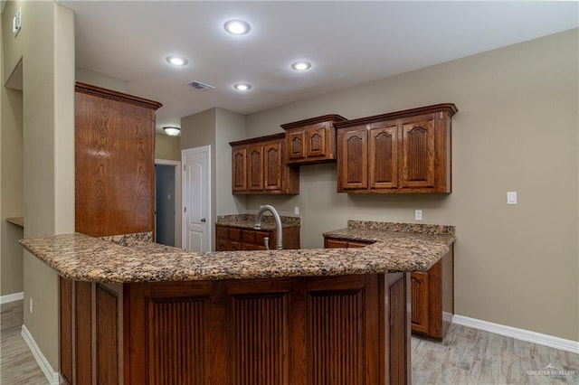 kitchen with dark stone countertops, kitchen peninsula, light hardwood / wood-style floors, and sink