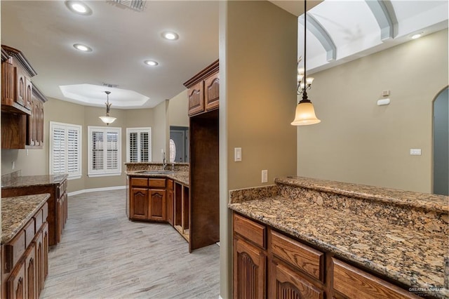 kitchen featuring sink, hanging light fixtures, dark stone countertops, light wood-type flooring, and a tray ceiling