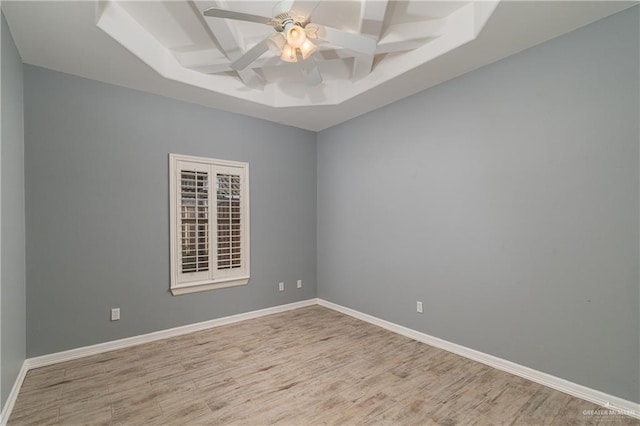 empty room with a tray ceiling, ceiling fan, and light hardwood / wood-style floors