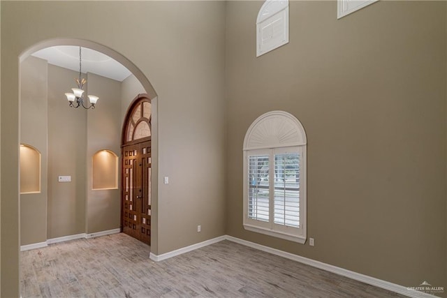 empty room with a towering ceiling, light wood-type flooring, and an inviting chandelier