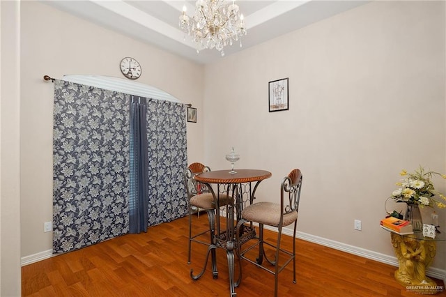 dining area featuring a raised ceiling, an inviting chandelier, and hardwood / wood-style flooring