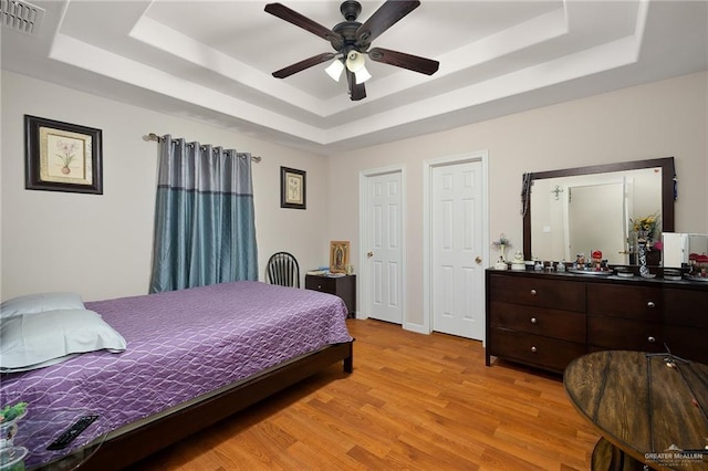 bedroom featuring ceiling fan, light hardwood / wood-style floors, and a tray ceiling