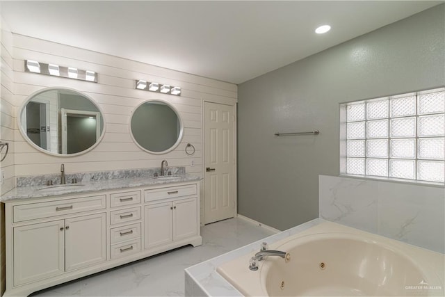 full bath featuring a whirlpool tub, marble finish floor, double vanity, and a sink