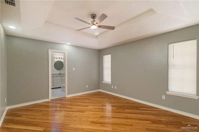 spare room featuring a raised ceiling, visible vents, ceiling fan, wood finished floors, and baseboards