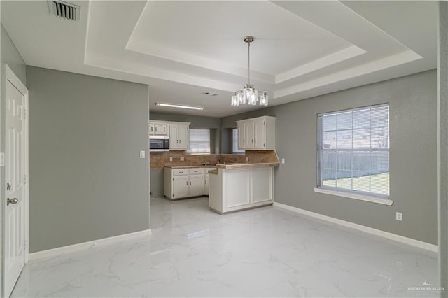 kitchen with a raised ceiling, stainless steel microwave, visible vents, white cabinets, and baseboards