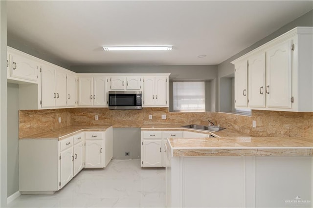 kitchen with marble finish floor, stainless steel microwave, white cabinets, a sink, and a peninsula