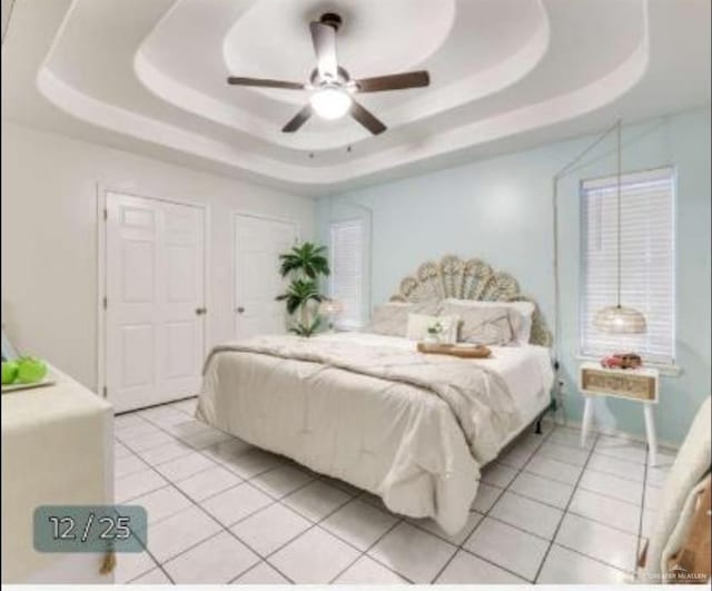 bedroom featuring a ceiling fan, a tray ceiling, and light tile patterned floors